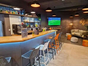A bar area with a counter, seating, a TV screen, and a variety of bottles. - ibis Rambouillet (Rambouillet)