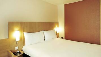 Ein Hotelzimmer mit einem großen Bett, zwei Nachttischen, einem Beistelltisch und einer Wandlampe.