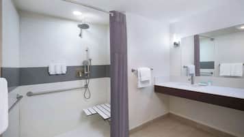 Un baño moderno con ducha, barra de apoyo, toallero y lavamanos con espejo.