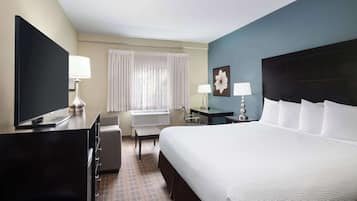 A hotel room with a bed, a desk, a chair, a TV, and a window with curtains.