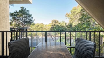 Een balkon met rieten stoelen en een tafel, met uitzicht op een parkeerplaats en bomen.