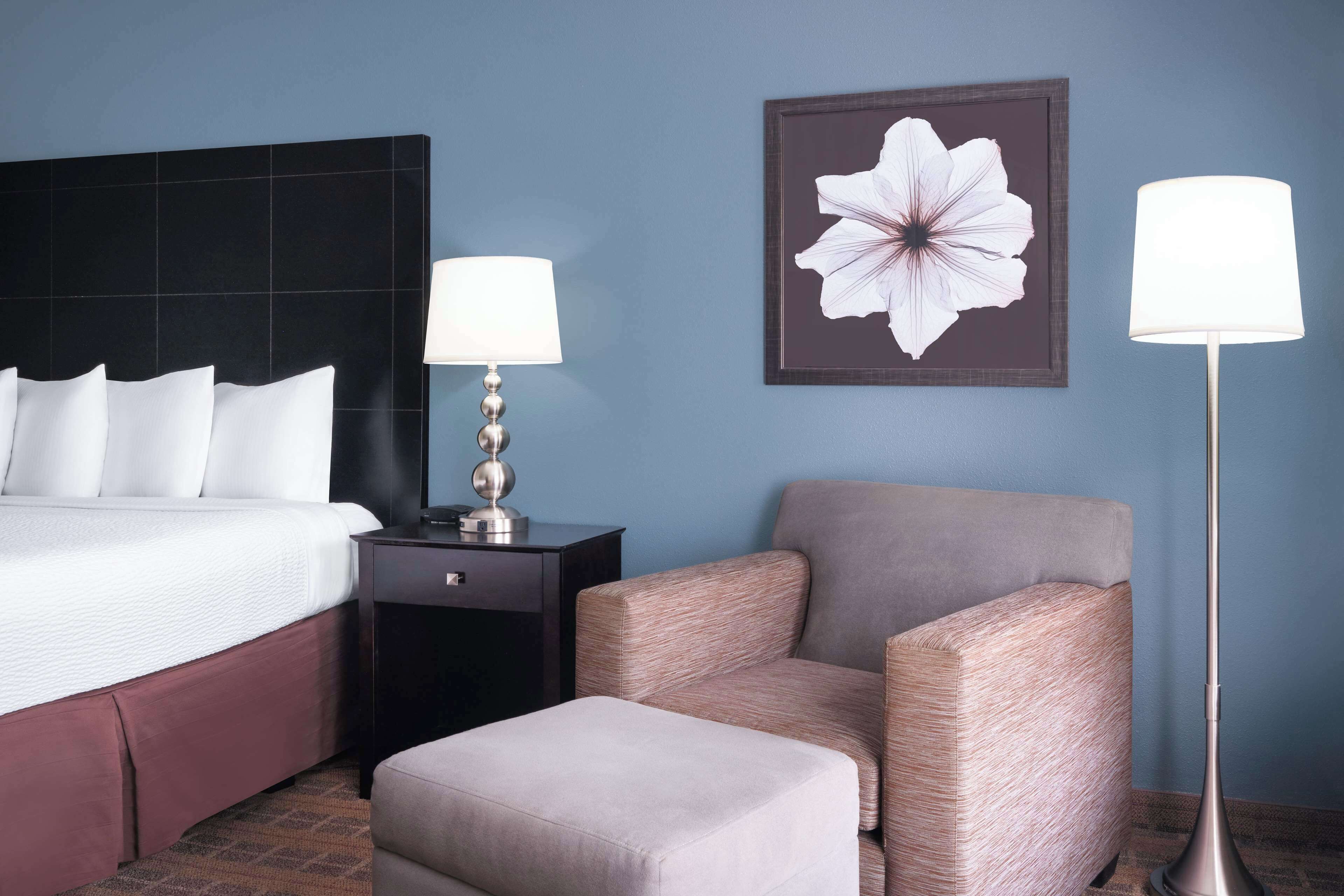 Una habitación de hotel con cama, mesita de noche, silla y reposapiés.