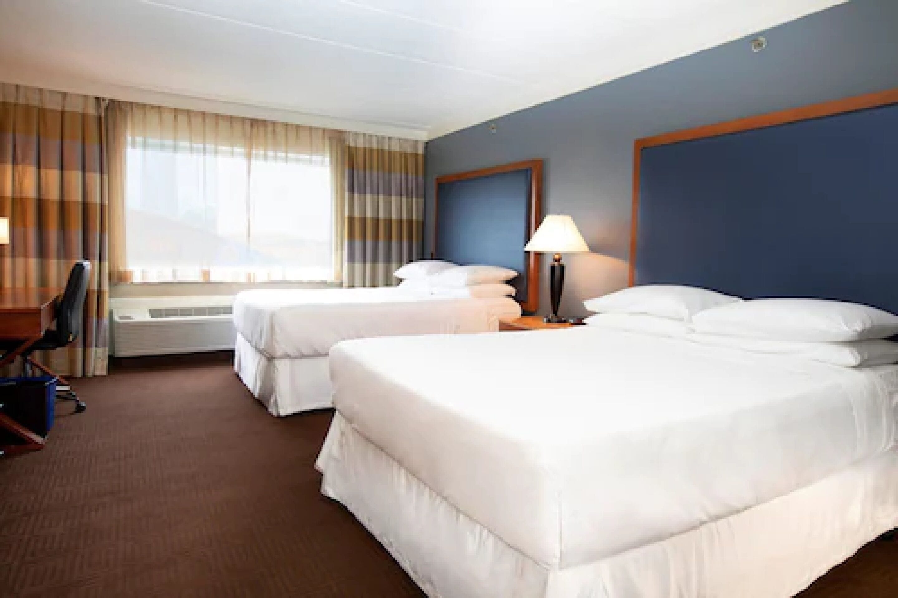 A hotel room with two beds, a desk, and a chair.
