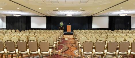 A large conference room with rows of chairs, a stage with a podium, and a large screen.