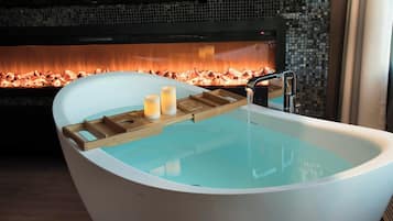 A modern bathroom with a freestanding bathtub, a wooden tray with candles, and a tiled wall with a mosaic design.