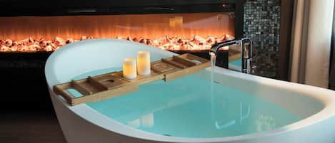 A modern bathroom with a freestanding bathtub, a wooden tray with candles, and a tiled wall with a mosaic design.