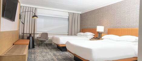 Una habitación de hotel con dos camas, un escritorio, una silla, un televisor y una ventana con cortinas.