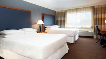 A hotel room with two beds, a desk, a chair, a lamp, and a window with curtains.