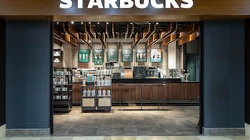 Uma Starbucks com interior moderno, detalhes em madeira e diversas opções de bebidas expostas em prateleiras.