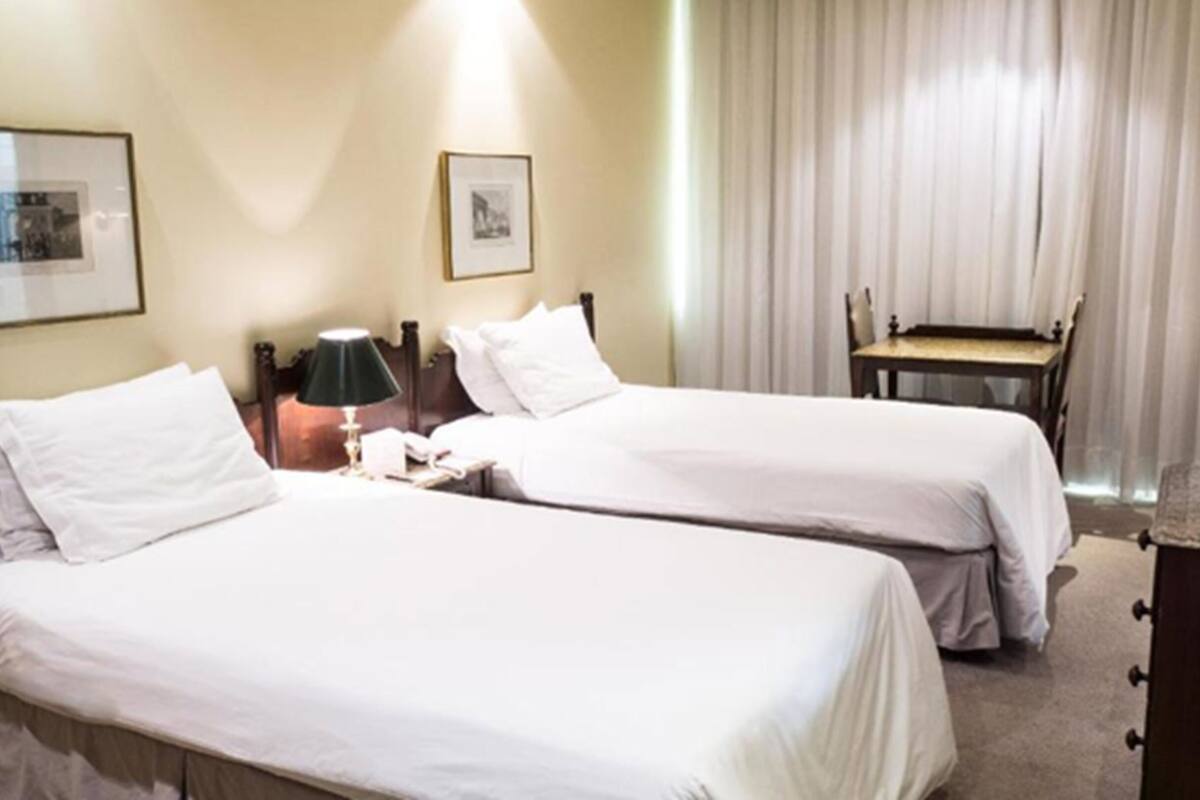 Camera d'albergo con due letti singoli, una scrivania con una sedia, una lampada e uno specchio.