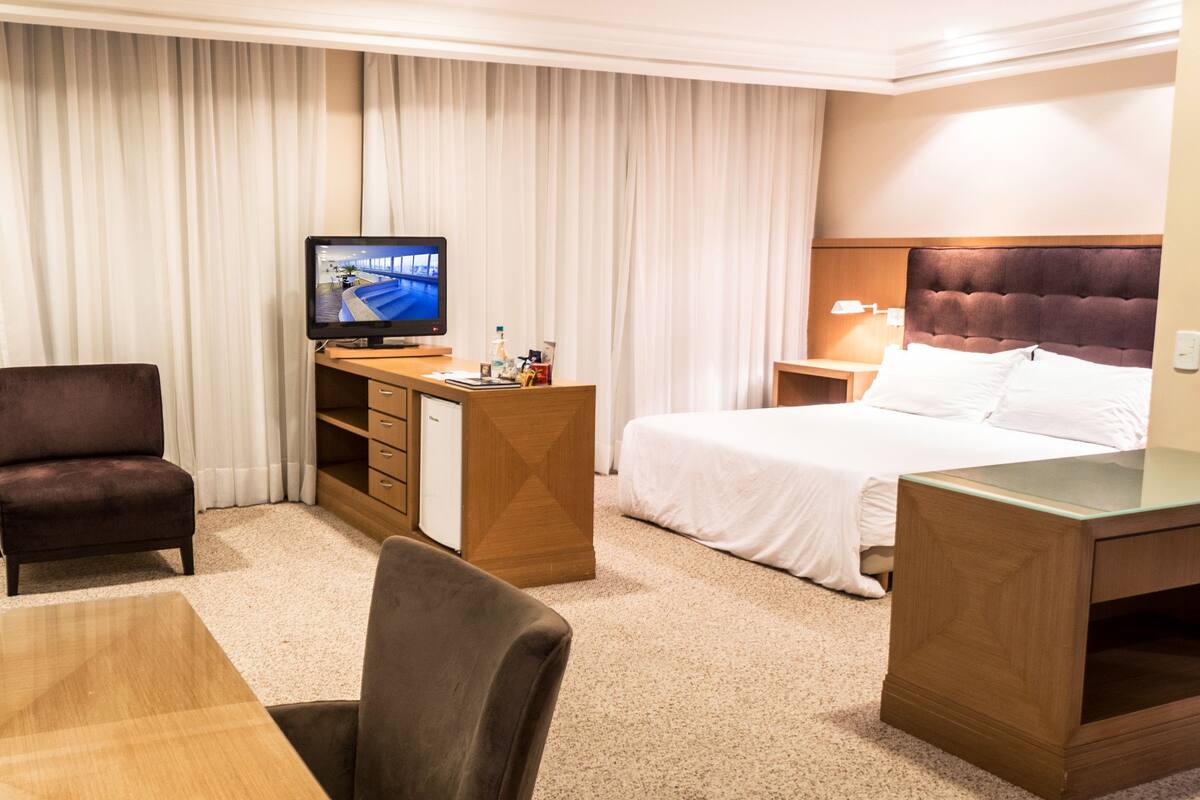 Una camera d'albergo con un letto, una scrivania, una sedia, una televisione e un minibar.