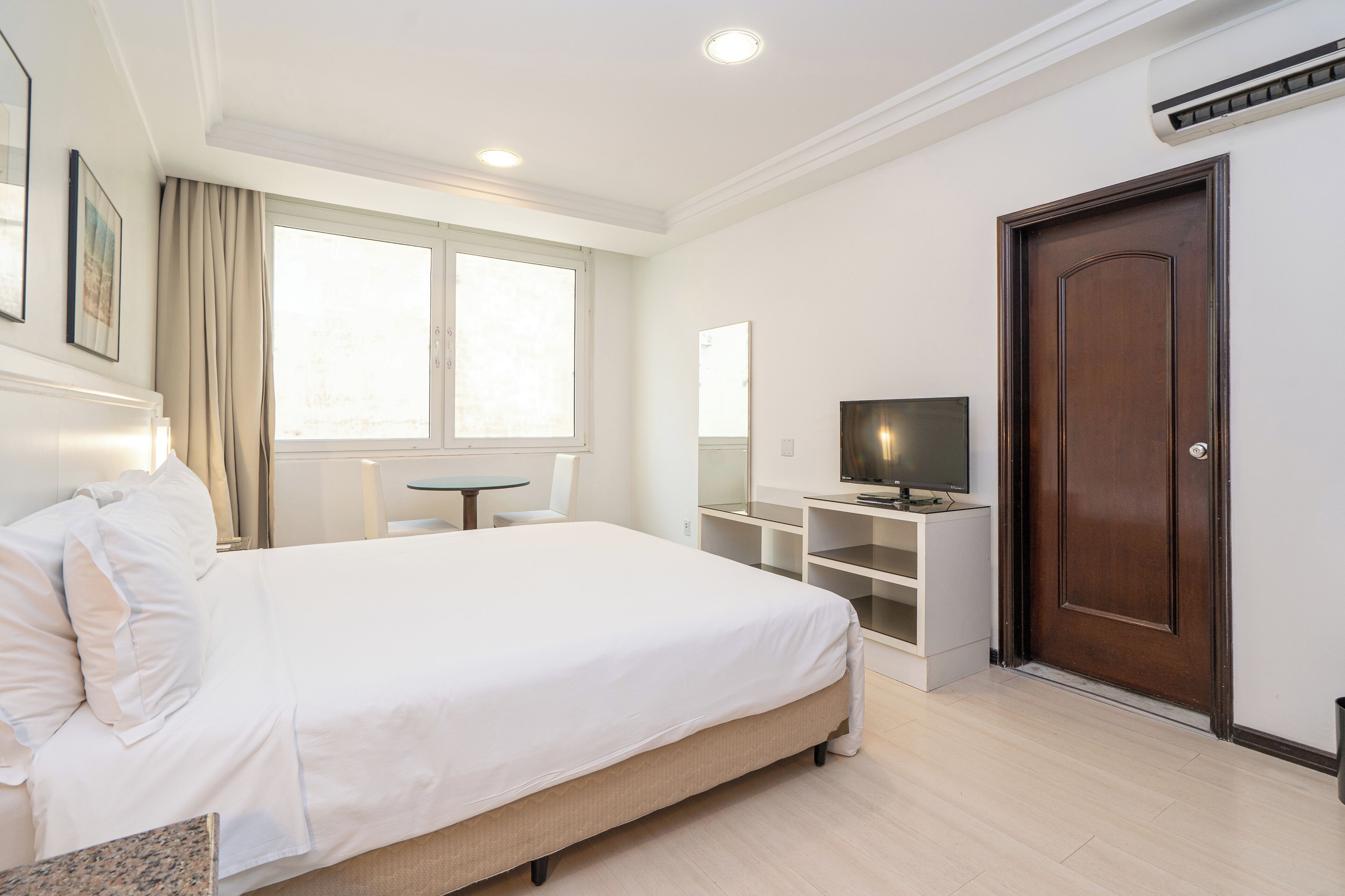 A hotel room with a bed, a desk, a television, and a door.