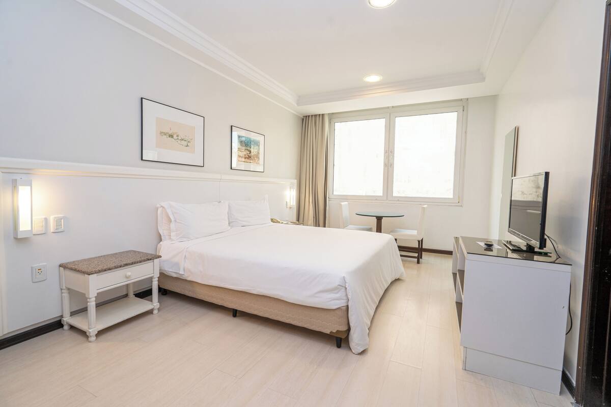 Una camera d'albergo con un letto, comodino, scrivania, televisore e opere d'arte alle pareti.