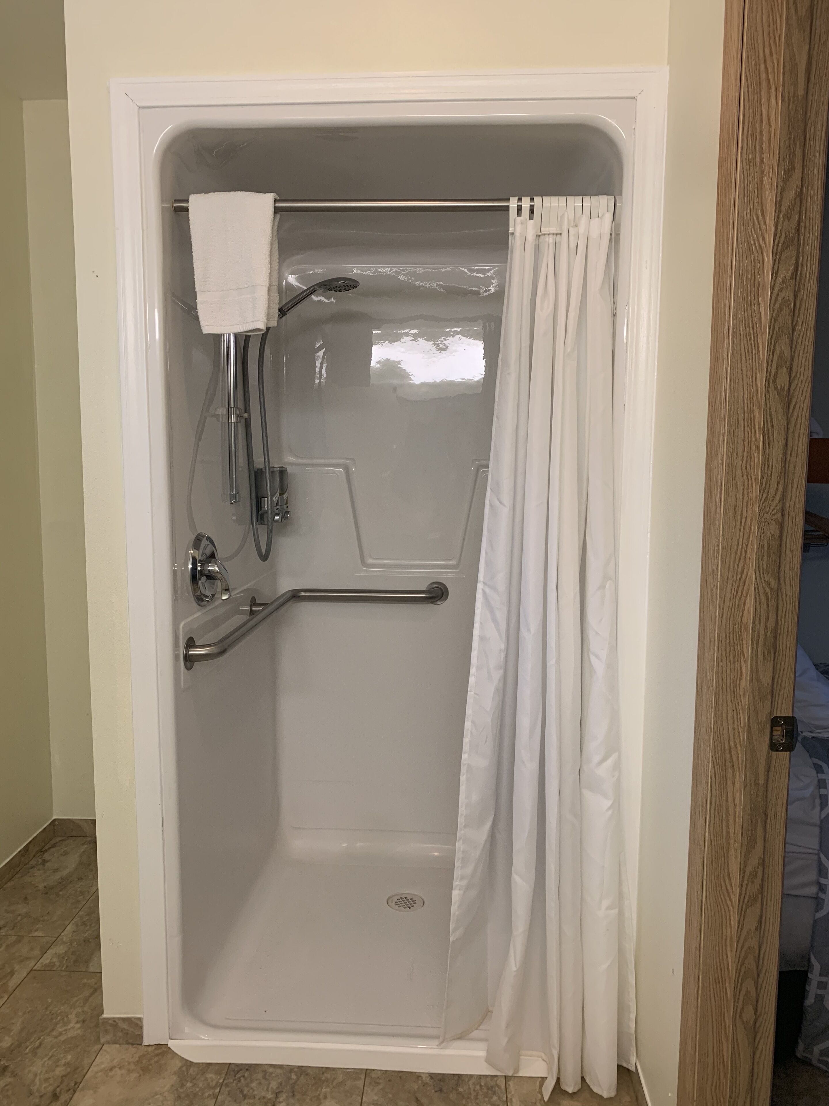 Une douche à l’italienne équipée d’une barre d’appui, d’un pommeau de douche amovible et d’un rideau blanc.
