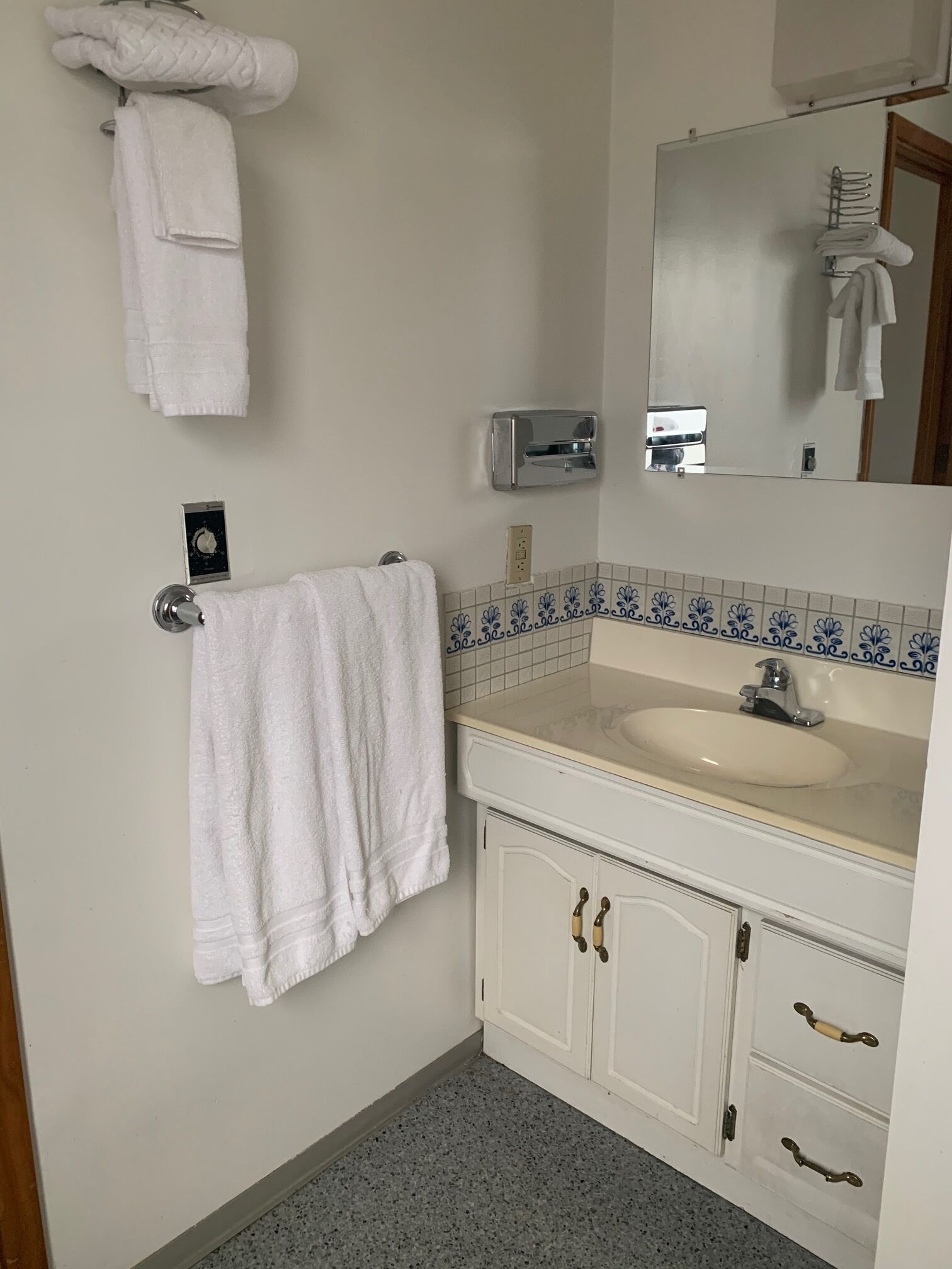 Un baño con un lavamanos blanco, un espejo y un perchero para toallas.