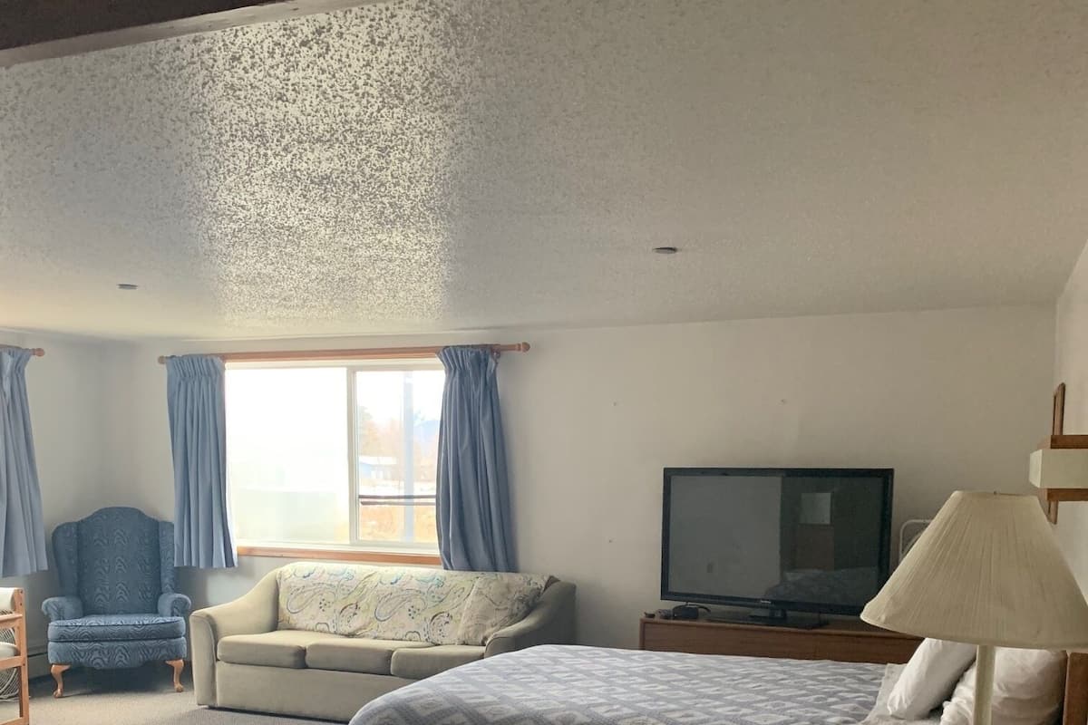 Quarto com cama, sofá, poltrona, televisão e abajur.