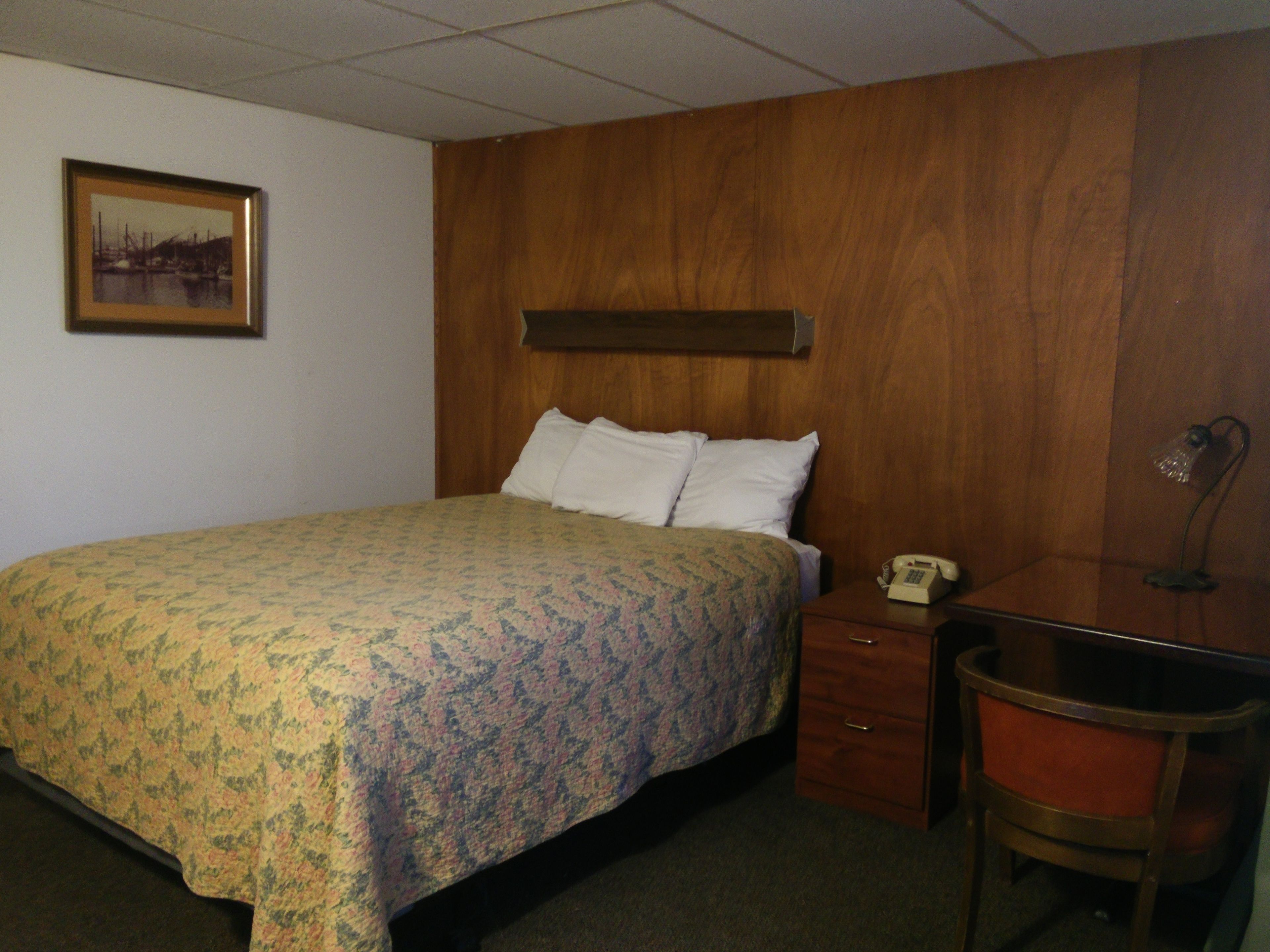 A hotel room with a bed, a nightstand, a desk, a chair, and a telephone.