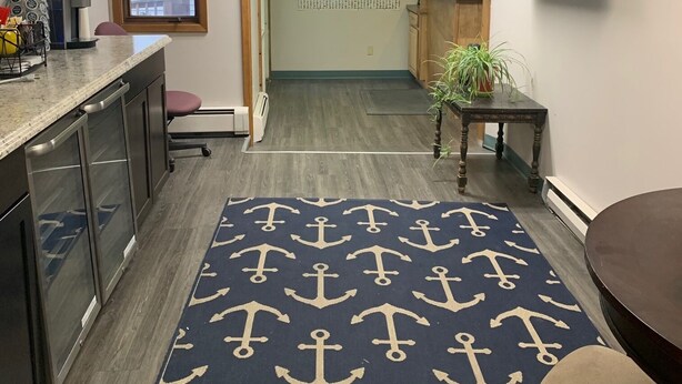 Un espacio de oficina moderno con área de cocina, un mapa mundial en la pared y una alfombra grande con motivos de anclas.