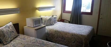 A hotel room with two beds, a microwave on a small table, a window with curtains, and a door.