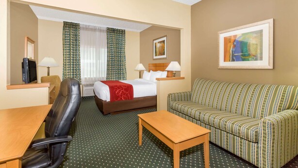 A hotel room with a bed, a sofa, a desk, a chair, and a television. - Baymont by Wyndham Billings (Billings)