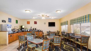 A hotel dining area with multiple tables and chairs, a kitchen area, and a ceiling fan. - Baymont by Wyndham Billings (Billings)