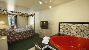 A hotel room with a bed, a television, a red bathtub, and a decorative wall. - Days Inn by Wyndham Riverside Tyler Mall (Riverside)