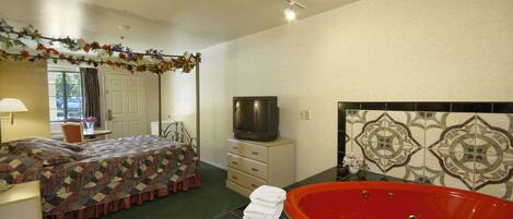 A hotel room with a bed, a television, a red bathtub, and a decorative wall.