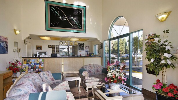 A lobby with a sofa set, a coffee table, a reception desk, and a large window with a view of the street. - Days Inn by Wyndham Riverside Tyler Mall (Riverside)
