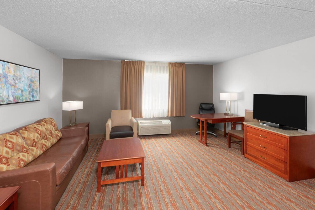 A hotel room with a sofa, a desk, a television, a chair, and a lamp.