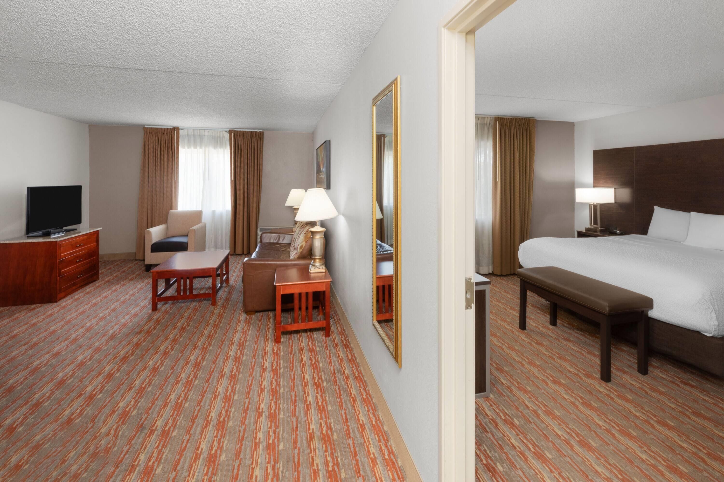 A hotel room with a bed, a desk with a television, a chair, a table with lamps, and a large mirror.