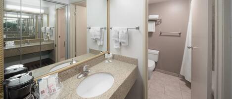 A hotel bathroom with a granite sink, a coffee maker, a mirror, and a toilet.