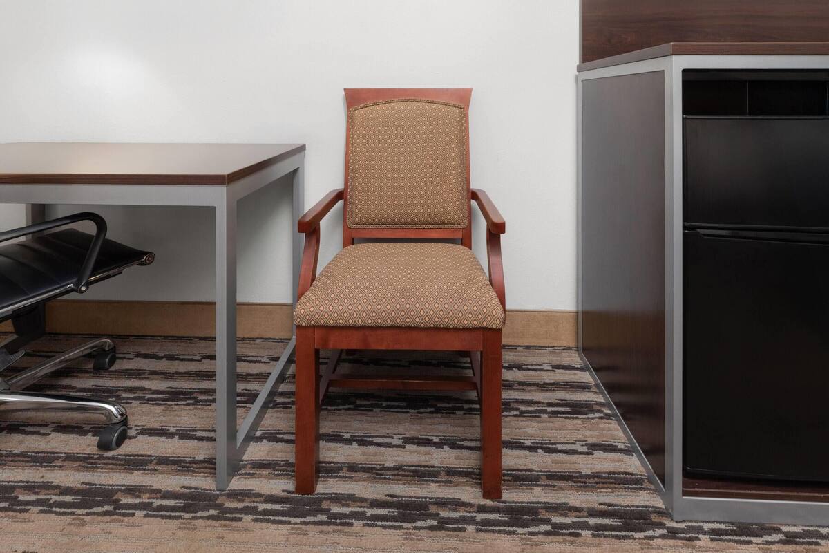 A chair with a patterned cushion, a table, and a refrigerator in a room with a patterned carpet.