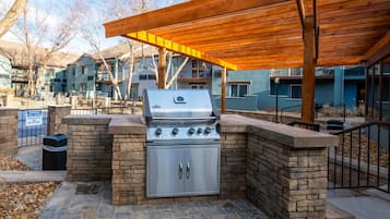 Una cocina al aire libre con parrilla, paredes de piedra y una pérgola de madera.
