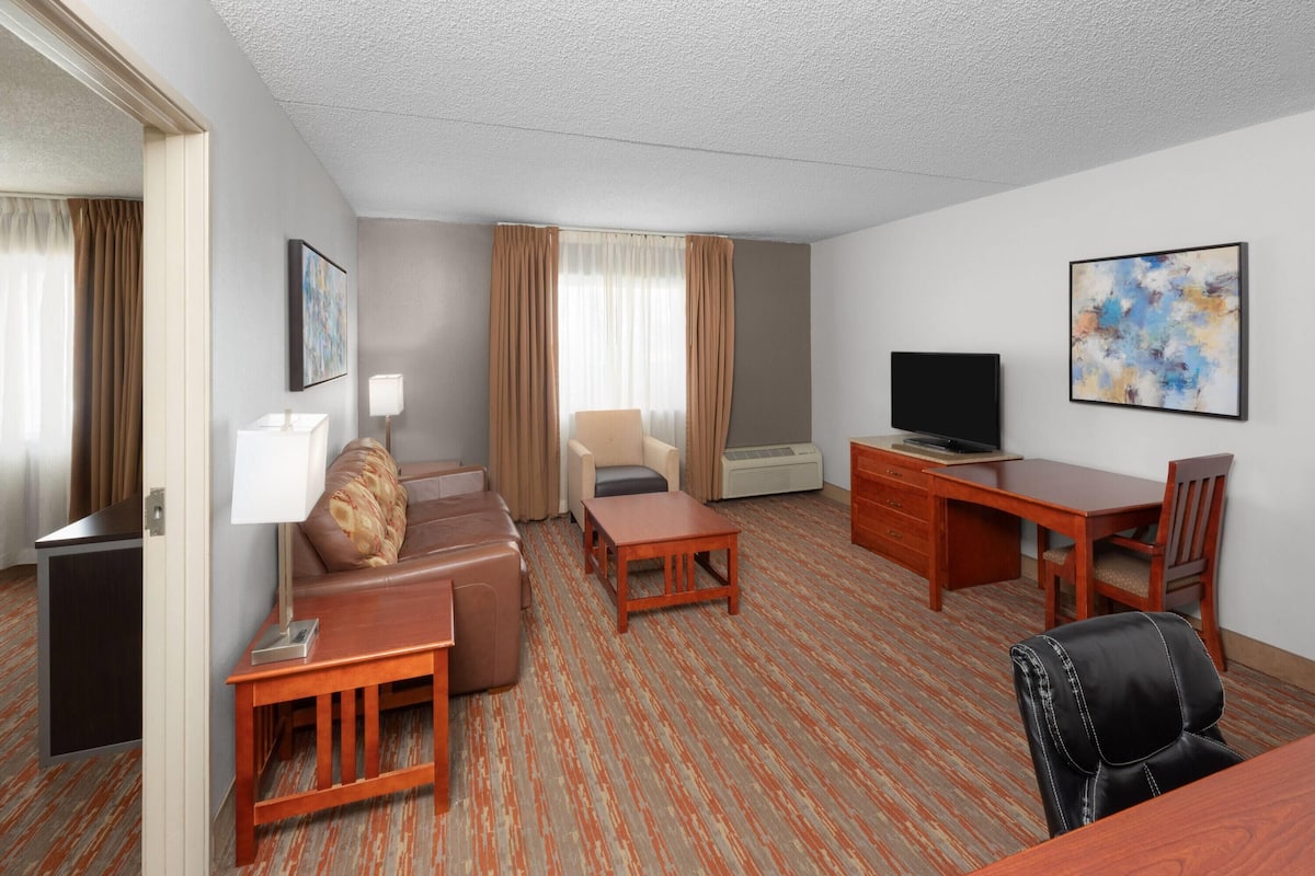 A hotel room with a sofa, a desk, a television, and a chair.
