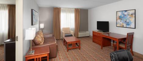 A hotel room with a sofa, a desk, a television, and a chair.