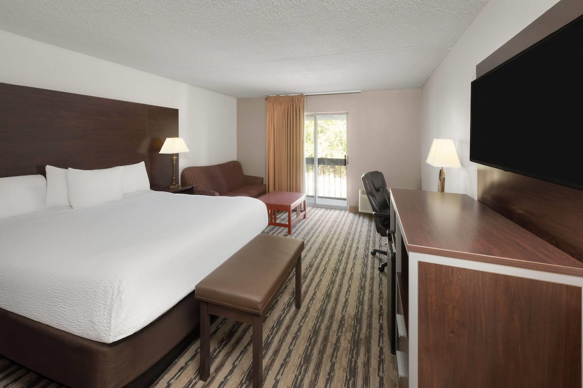 A hotel room with a large bed, a desk, a chair, a TV, and a window with curtains.