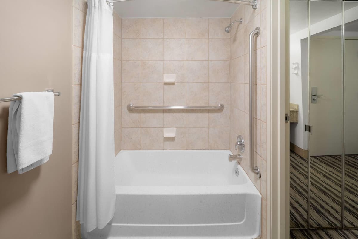 A walk-in shower with a grab bar, a white towel, and a soap dish.