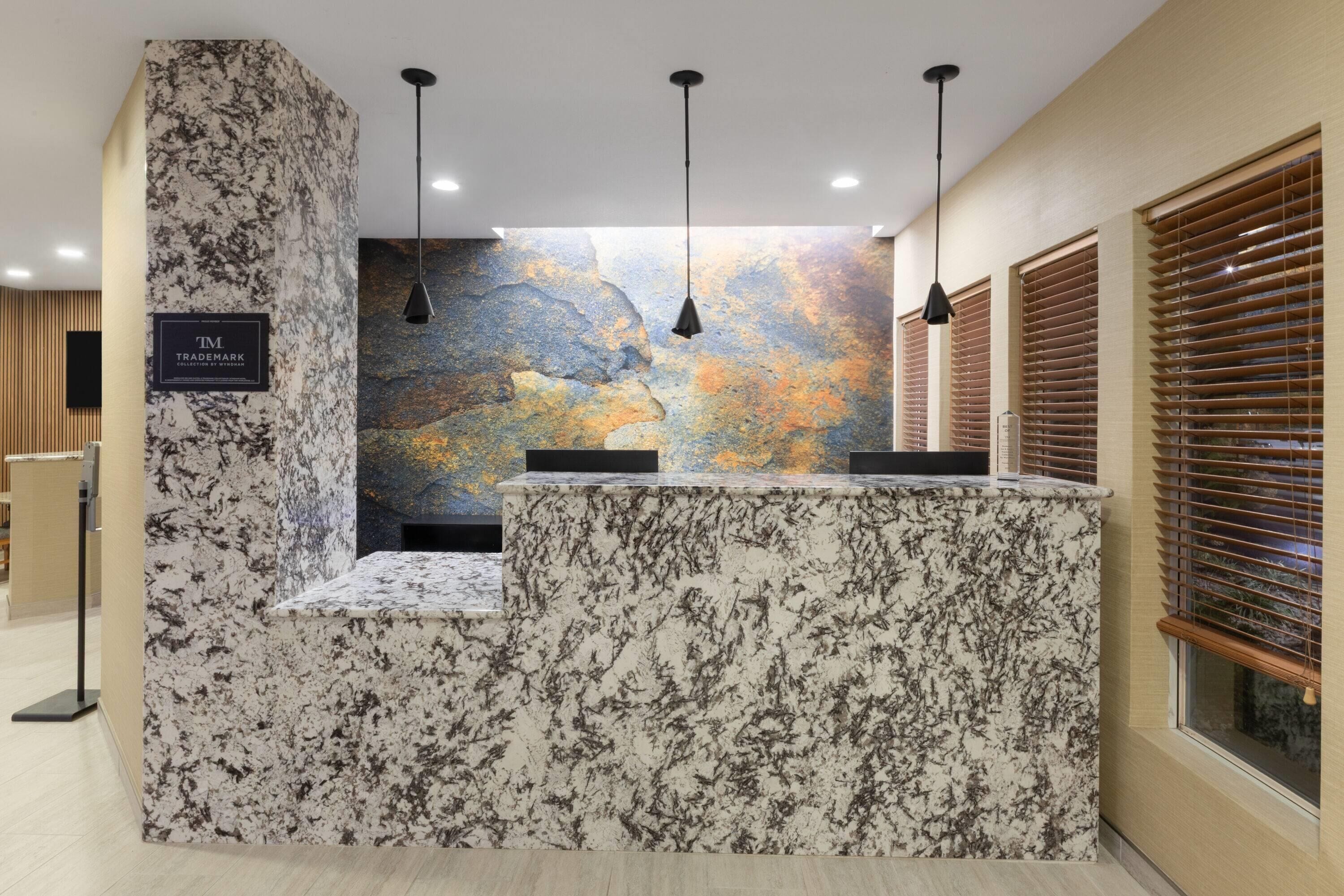 A reception desk with a marble top, a wall mural, and wooden blinds.