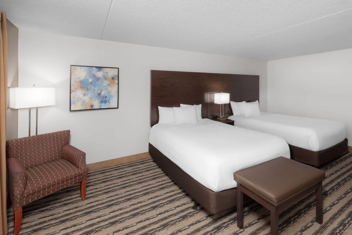 A hotel room with a large bed, a smaller bed, a sofa, a nightstand, a lamp, and a painting on the wall.