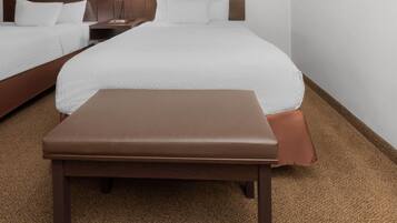 A hotel room with two beds, a bench, and a nightstand with a lamp.