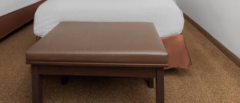 A hotel room with two beds, a bench, and a nightstand with a lamp.
