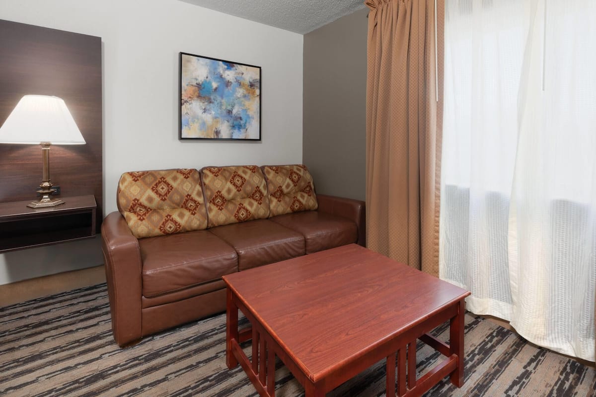 A living room with a brown leather sofa, a wooden coffee table, a lamp, and a painting on the wall.