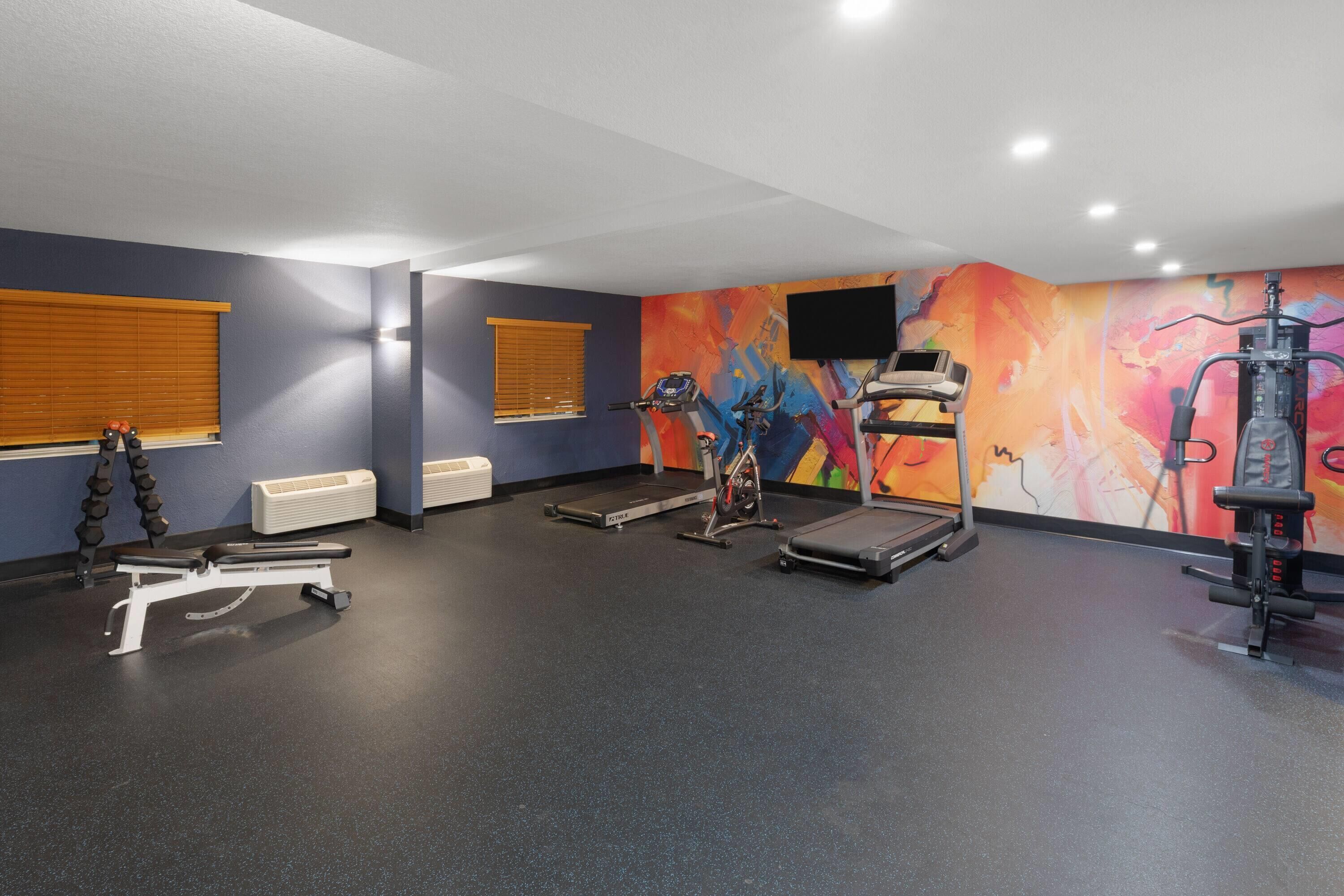 A gym with exercise equipment, a treadmill, and a wall-mounted TV.