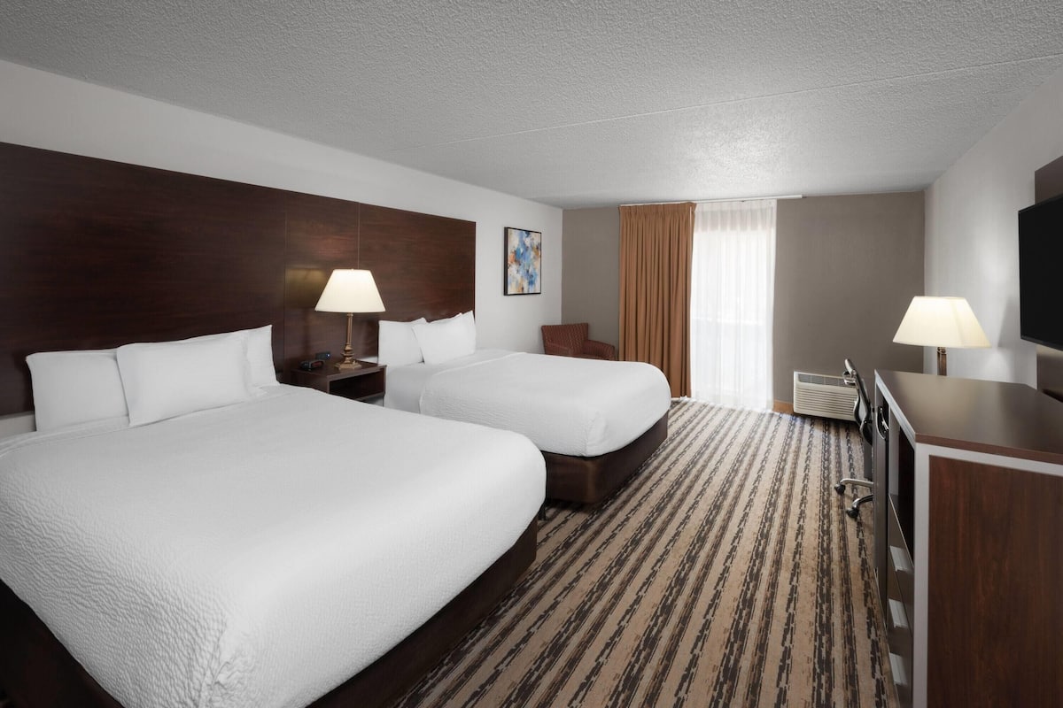 A hotel room with two beds, a desk, a TV, and a window with curtains.