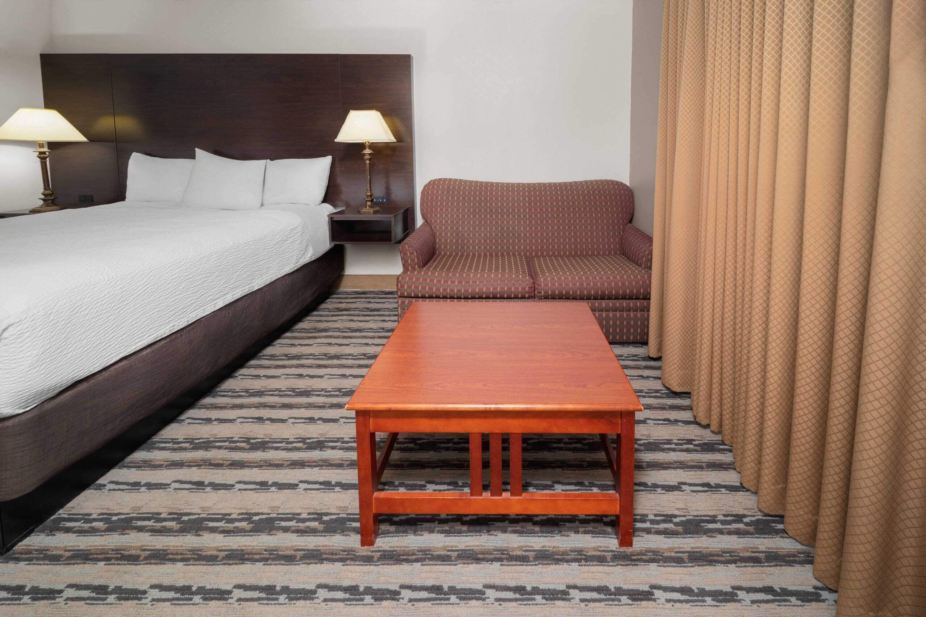 Ein Hotelzimmer mit einem großen Bett, einem Holztisch, einer gemusterten Couch und einem Teppich mit Muster.