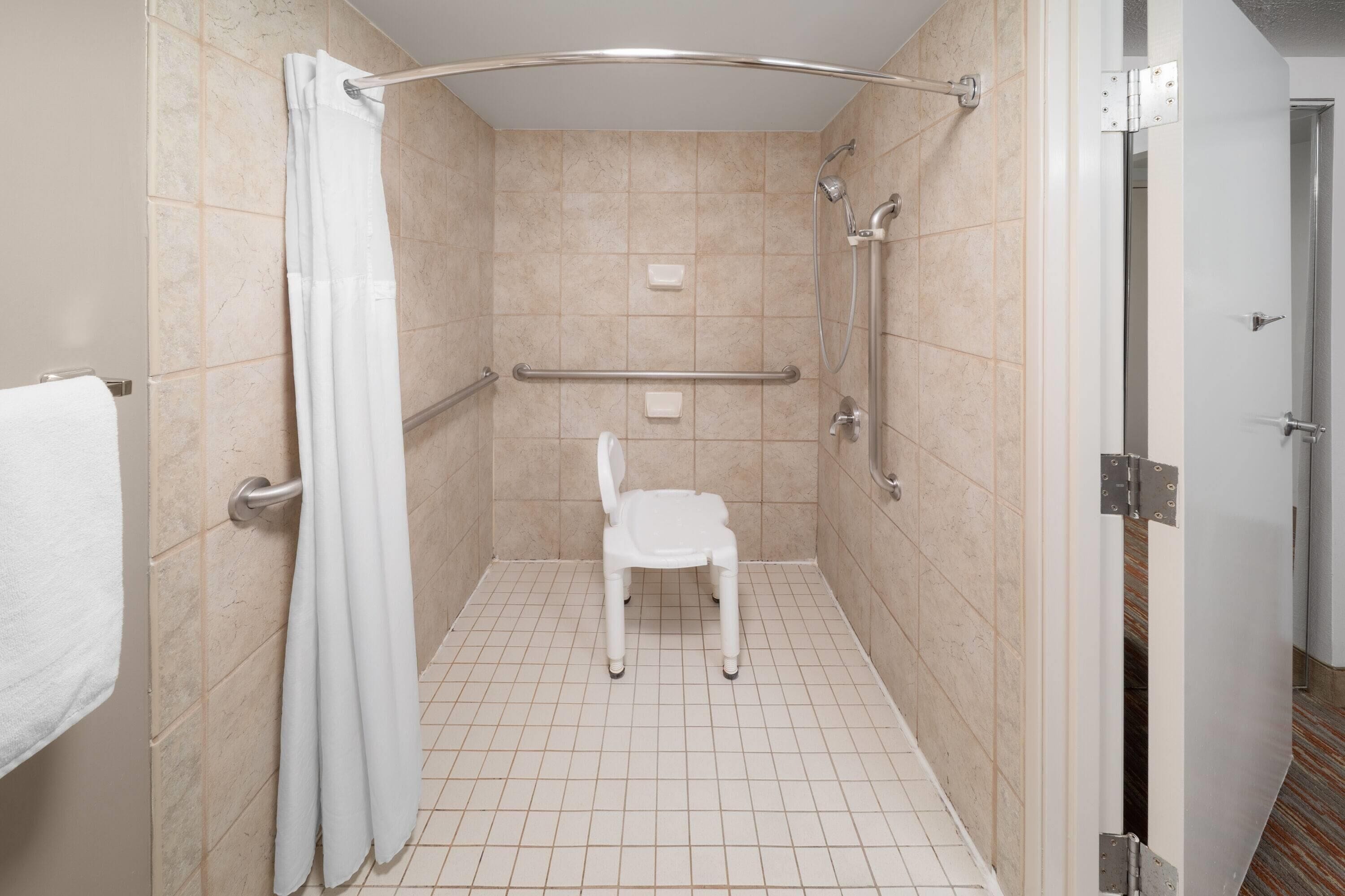 A small, enclosed shower area with a white chair, a grab bar, and a shower curtain.