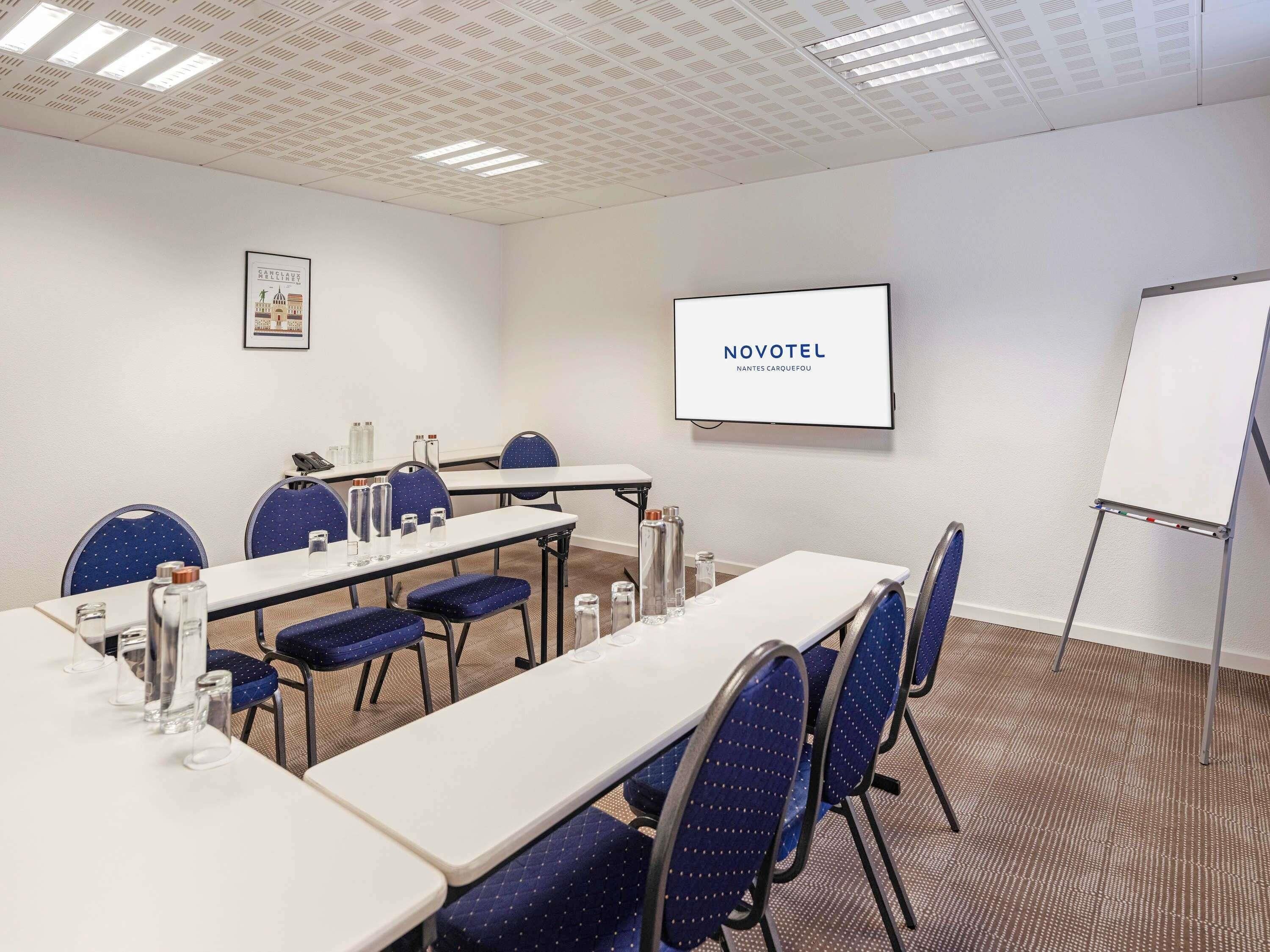 Ein Konferenzraum mit Tischen, Stühlen, einer Projektionsleinwand und einer Whiteboard-Tafel.