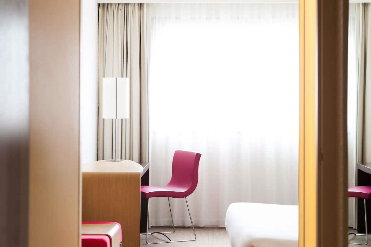 Habitación de hotel con cama, escritorio, silla y lámpara.