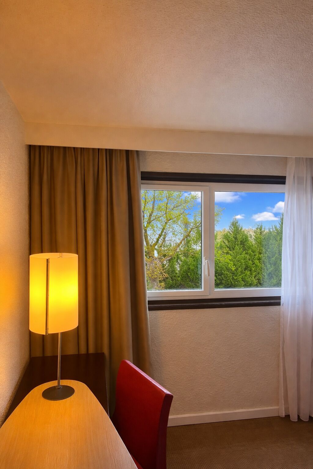 Une pièce avec une fenêtre, une lampe, une chaise et un sol recouvert d’une moquette.