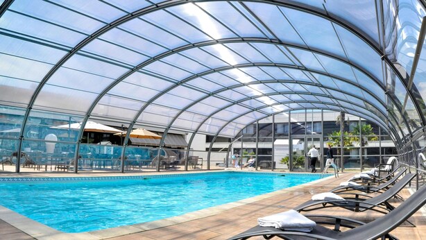 Una piscina techada con sillas de descanso y una estructura de techo de vidrio.